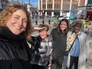 Franca Roeschert along with Nic Dickson, Binki Taylor and Catriona Macleod out on a walk around Brixton. Franca is smiling whilst holding the camera. The other team members are also smiling. It is a bright and sunny day.