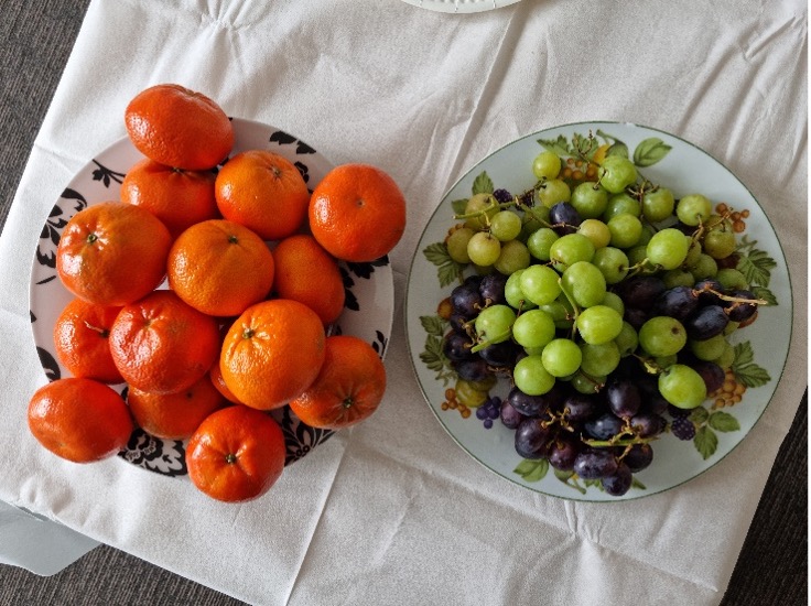 Oranges and grapes placed in two decorative bowls, which sit on a white table cloth.