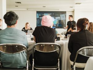 Three people sat in a meeting facing their speakers. We can see them from the backs of their heads.