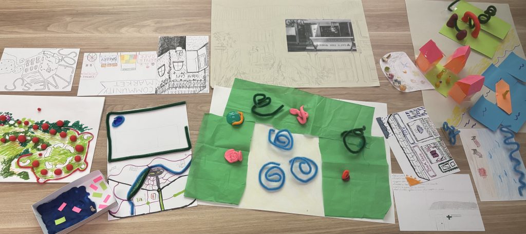 A selection of work from the town planning workshop, featuring crafts, drawings, models and sketches laid out on a table.